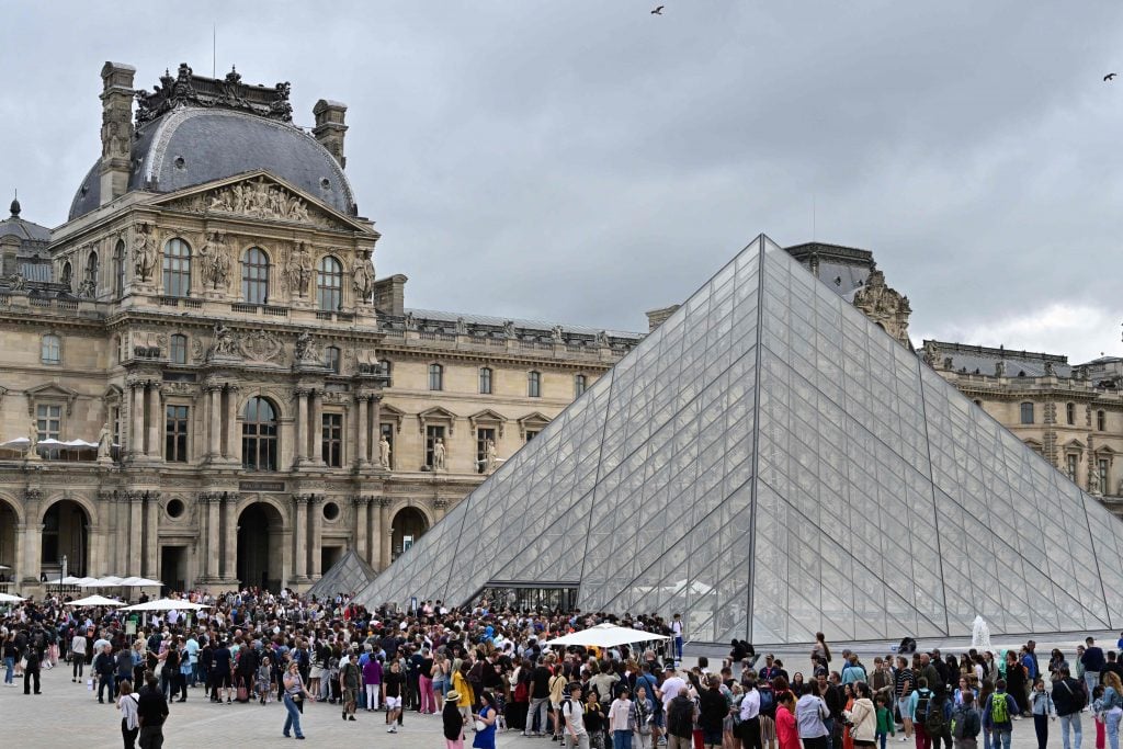 photograph of the exterior of the louvre museum with condensed crowd of visitors out front