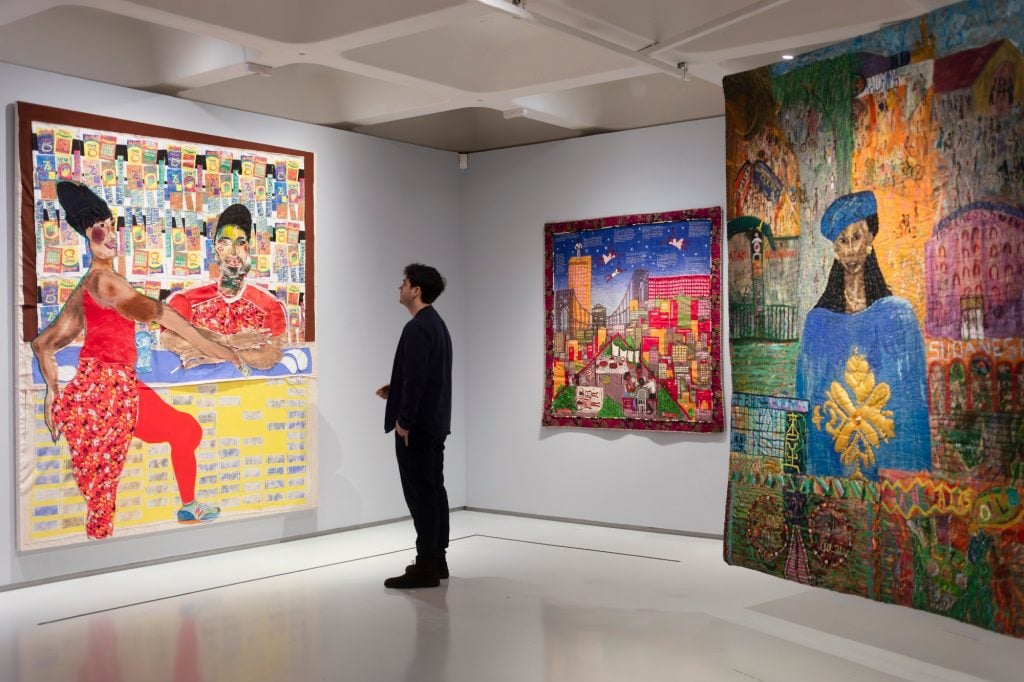 A man looks at textiles hanging in an art gallery