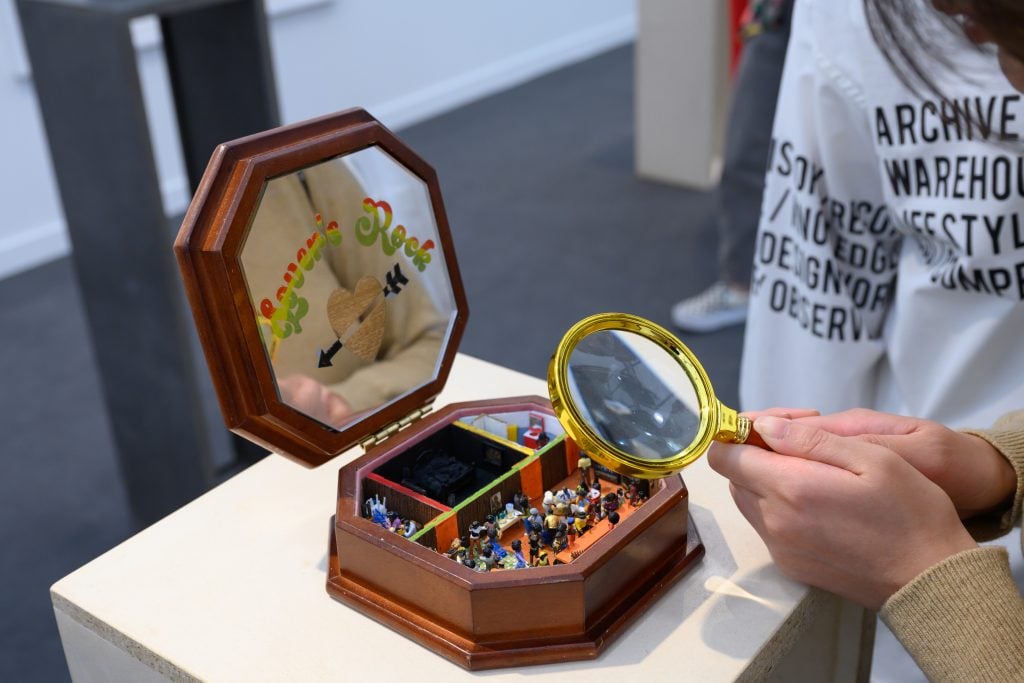 A person looks through a magnifying glass at a tiny sculpture on display at Frieze in Los Angeles.