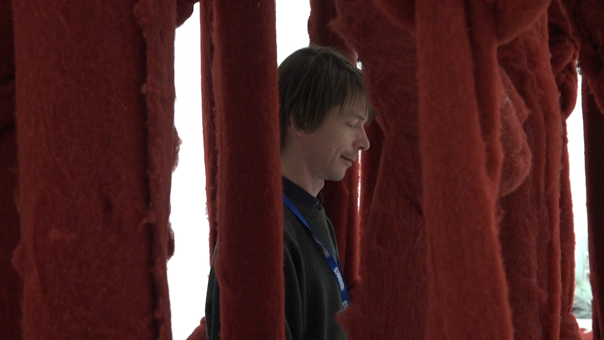 Curator Adam Szymczyk walks between the long strands of a hanging sculpture by Cecilia Vicuña