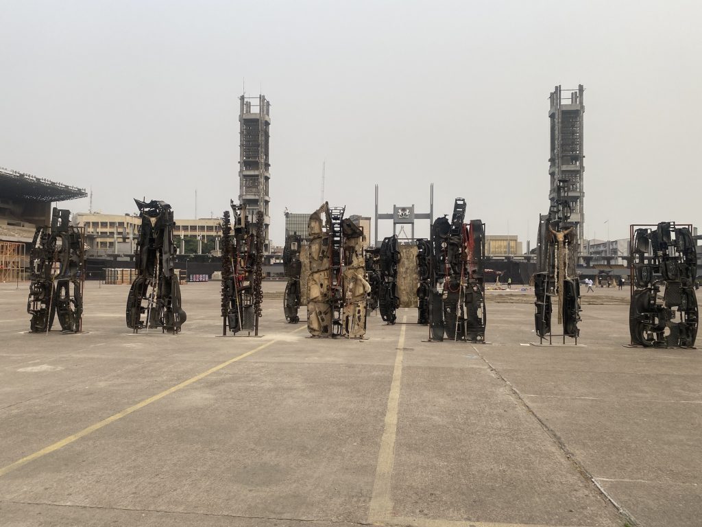 A series of seven monolith sculptures in a plaza, made from car parts
