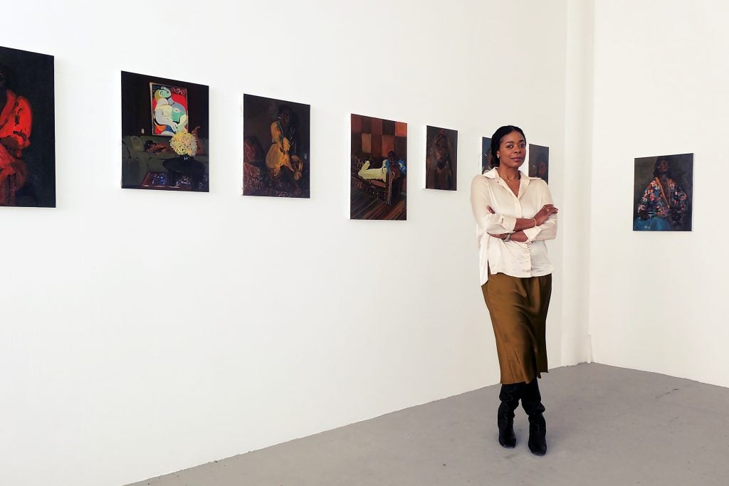 Portrait of a woman in front of her paintings in a gallery space