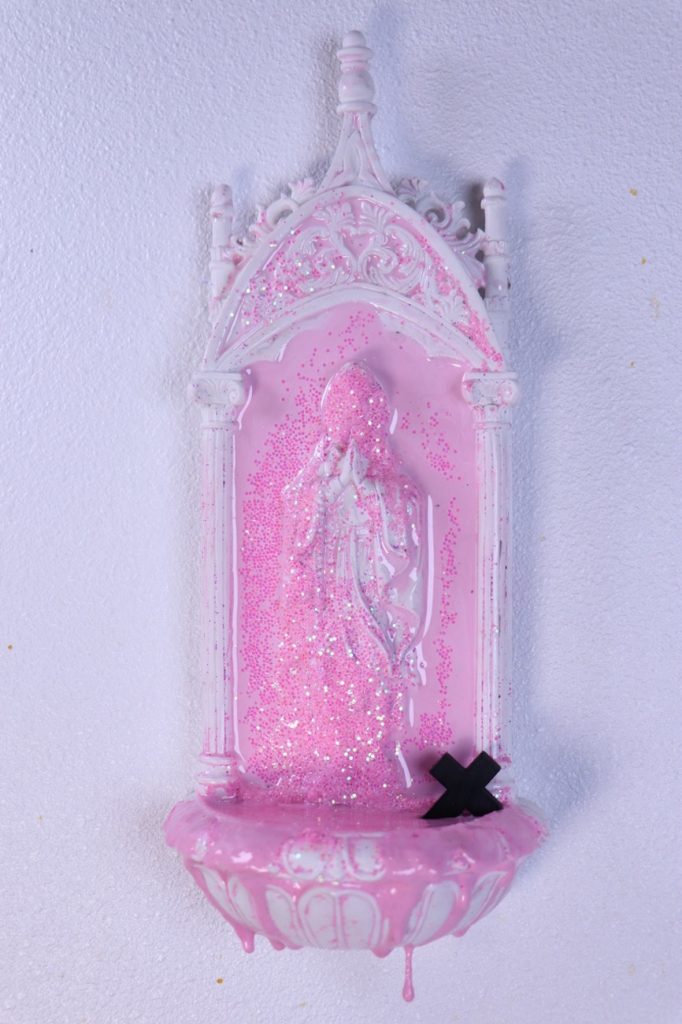 An artwork made of a holy water dispenser covered with pink paint and glitter