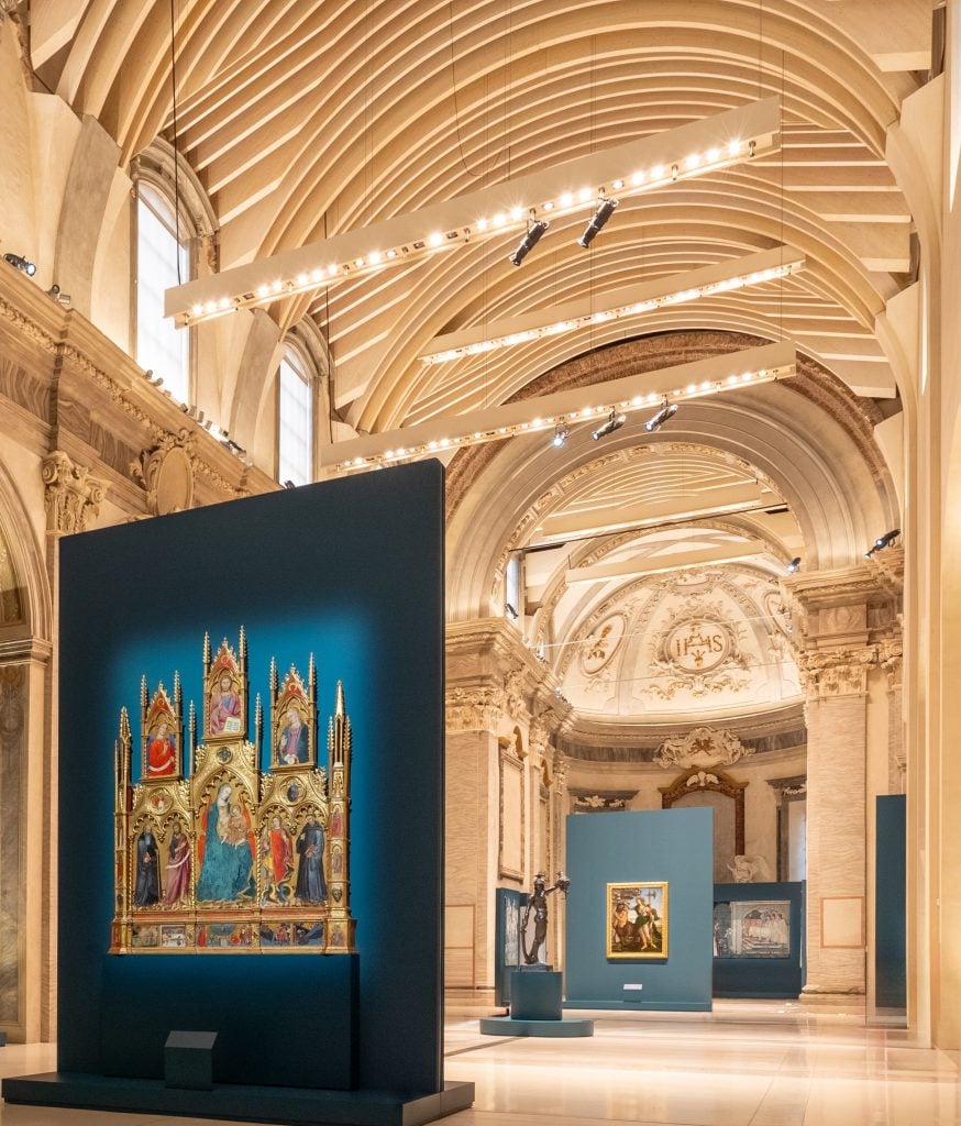An architectural space with dramatic arches has paintings and sculptures on view.