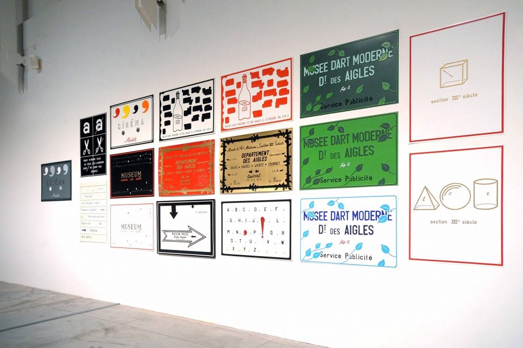 A room hung with placards designed with text and art by artist Marcel Broodthaers.