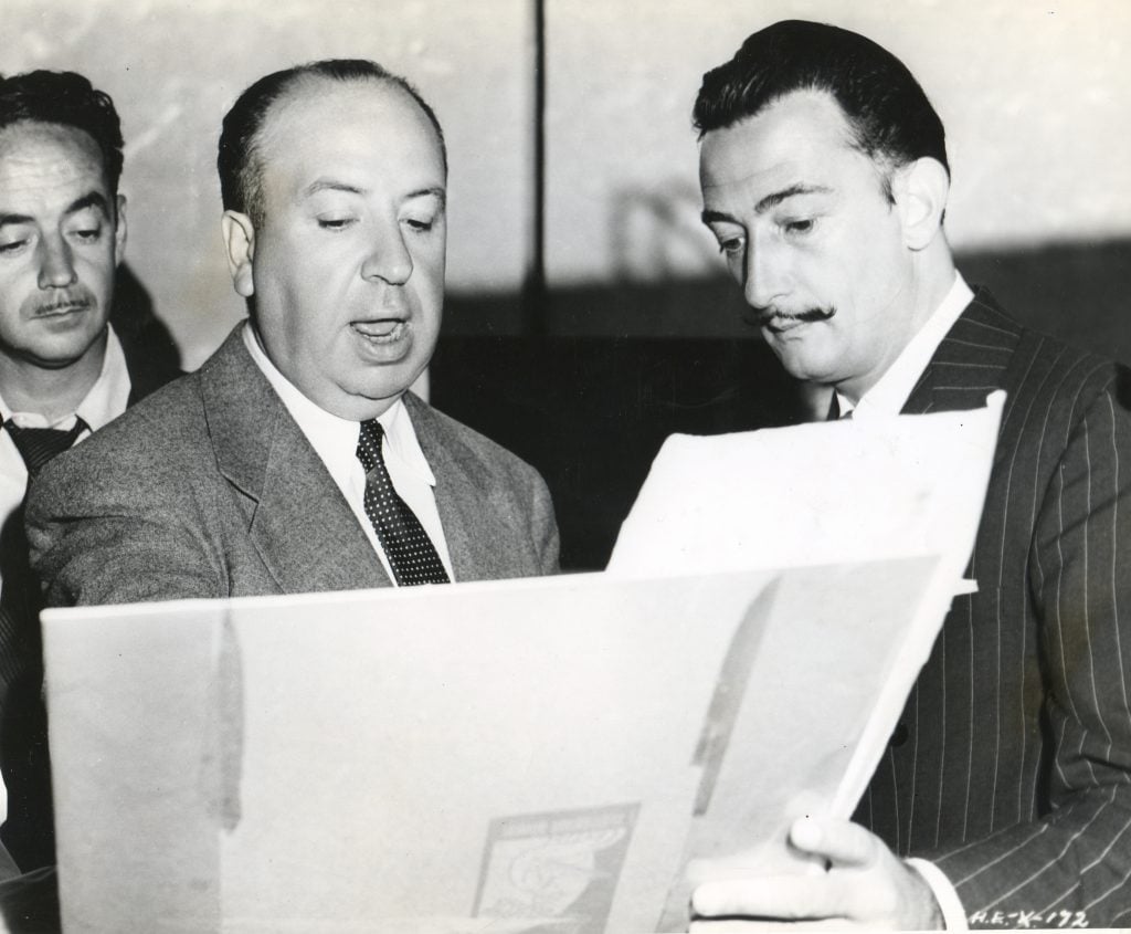A black and white photo of two men standing side by side, both examining storyboards