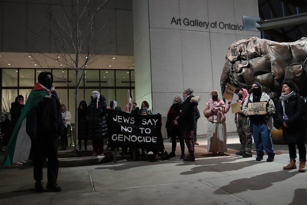 Protestors stand outside of a museum holding signs that read 'Jews say no to genocide,' 'free gaza,' and 'free palestine' 