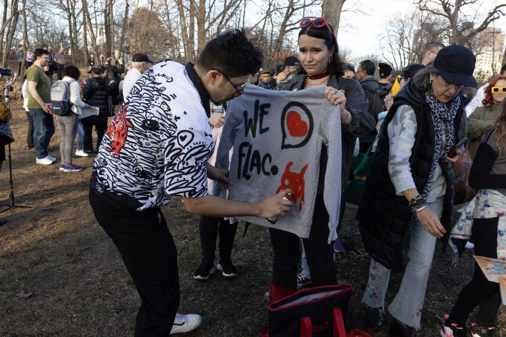 In the foreground, a person is holding up a gray sweatshirt with the words 