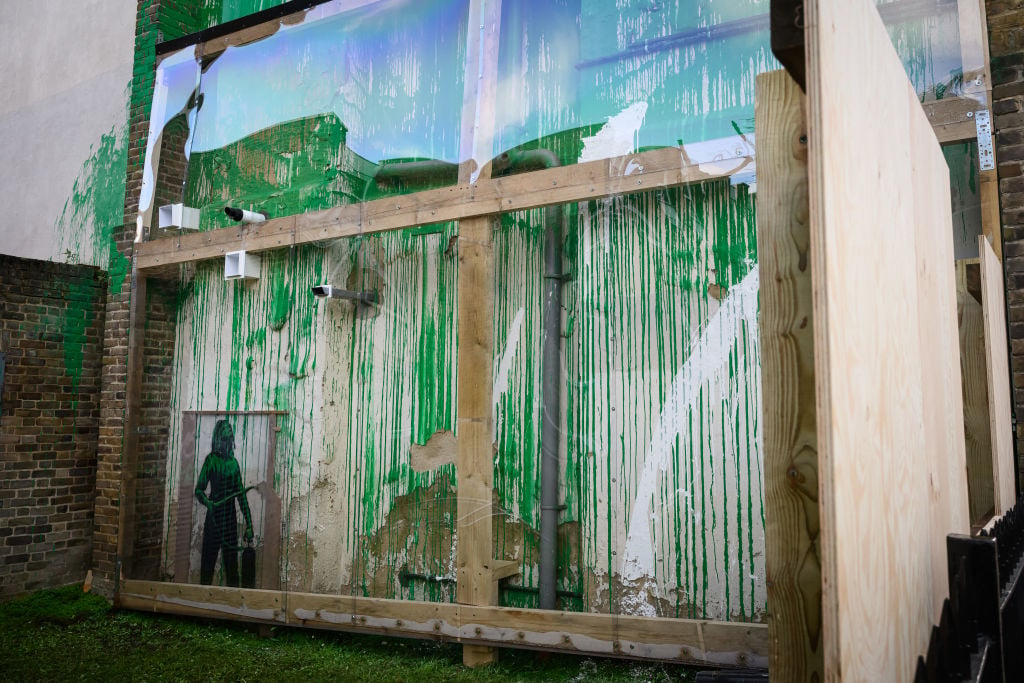 a brick building wall splashed with green and white paint is covered with har plastic sheeting