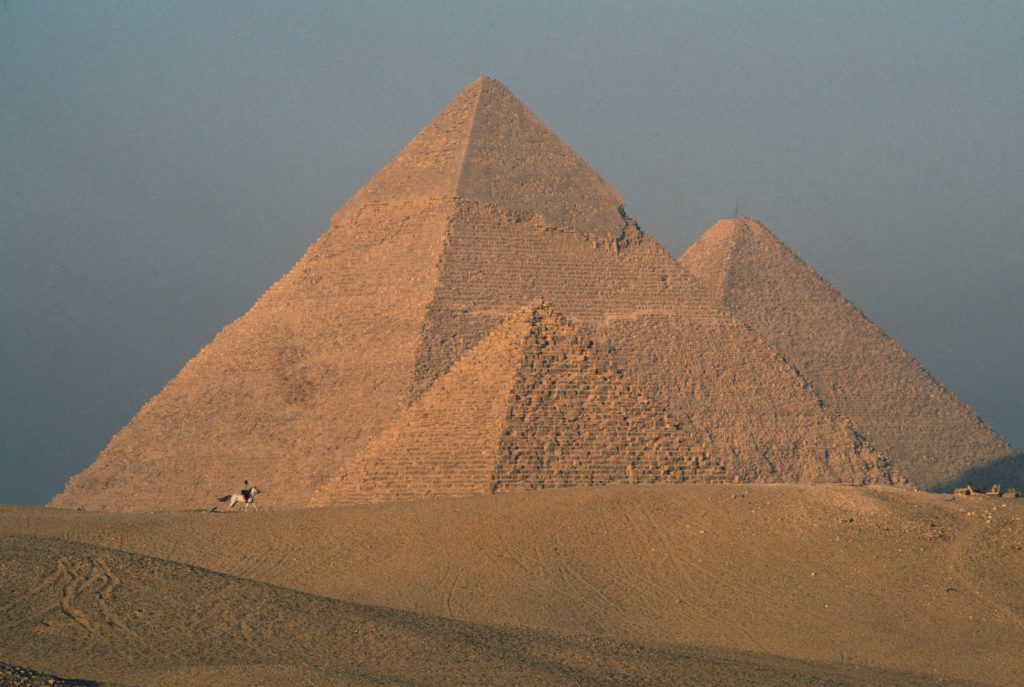 Three Egyptian pyramids framed against a cloudy, grey sky.