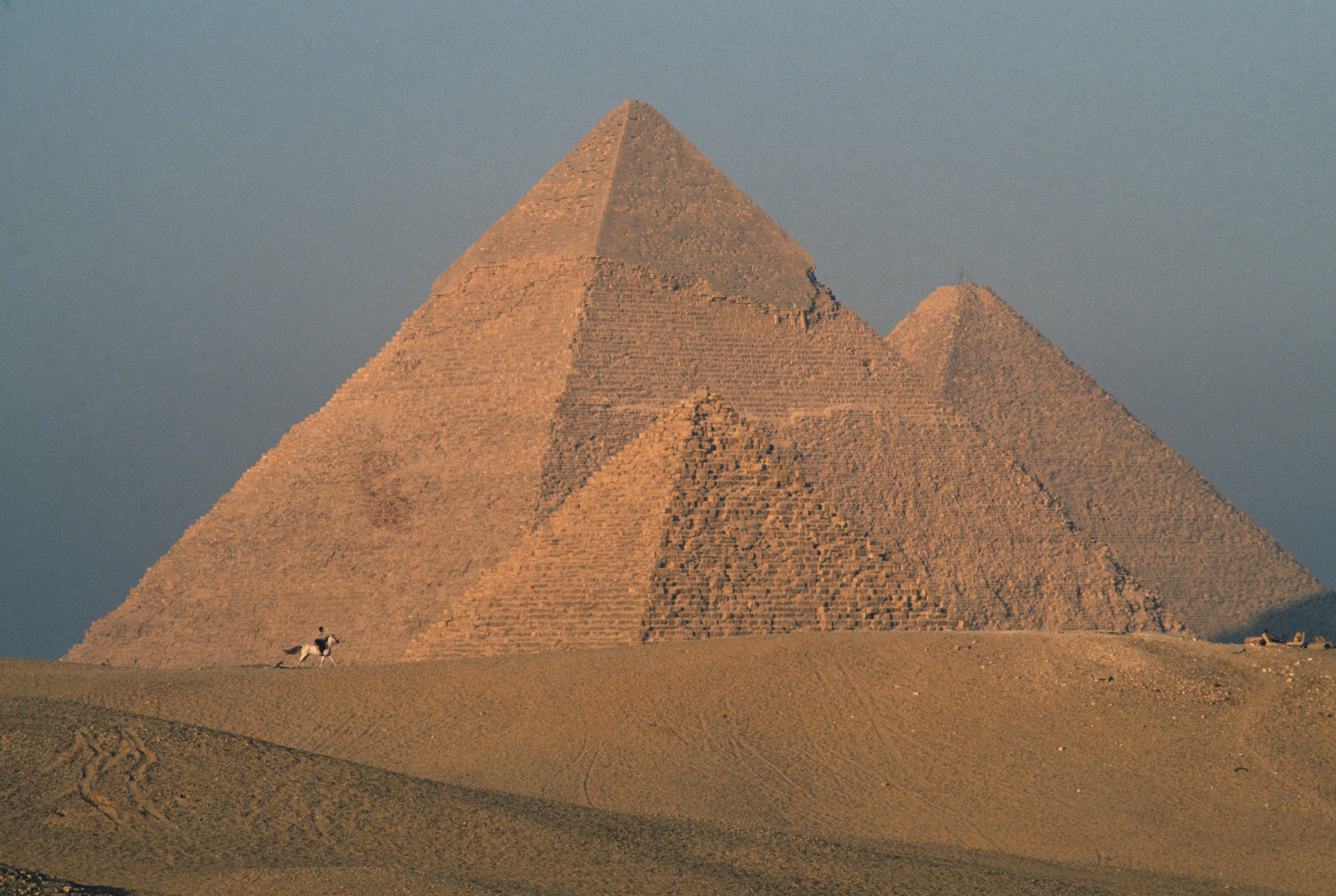 Three Egyptian pyramids framed against a cloudy, grey sky.