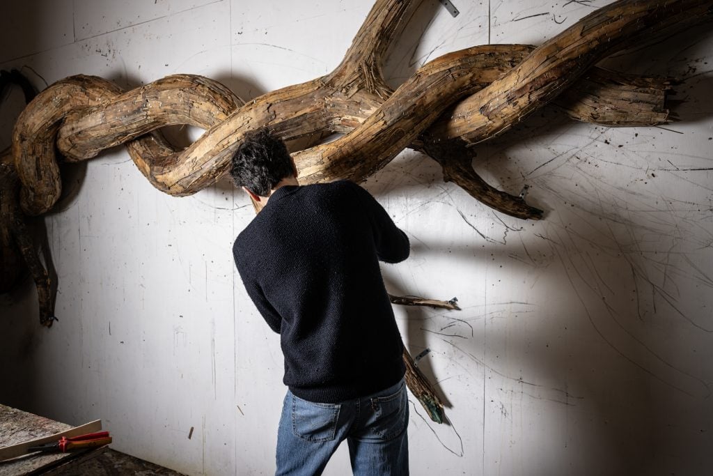 a man is shown with his back away from us working on a sculpture that looks like the intwined branches of a tree