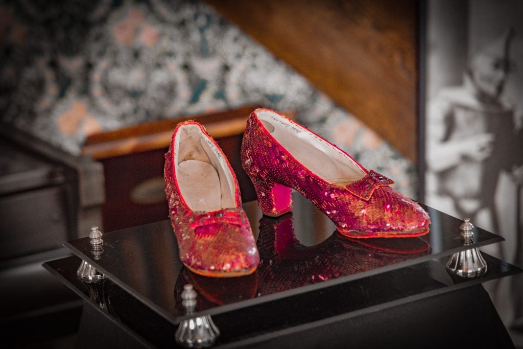 A pair of red shoes, sewn with red sequins, on a display platform.