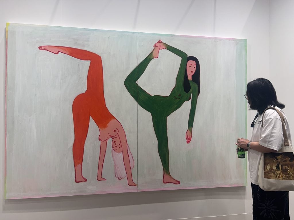 a man stands in front a a painting of two women doing stretch exercises at an art fair 