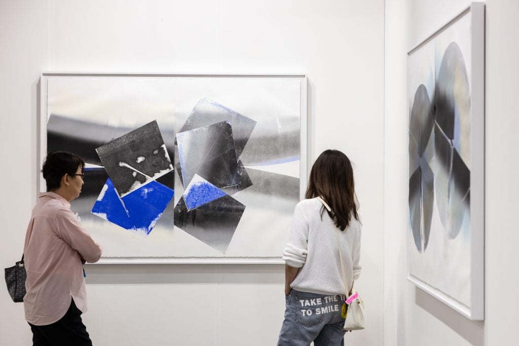 In a color photo, two people stand amid two white walls that each hold a black-on-white painting.