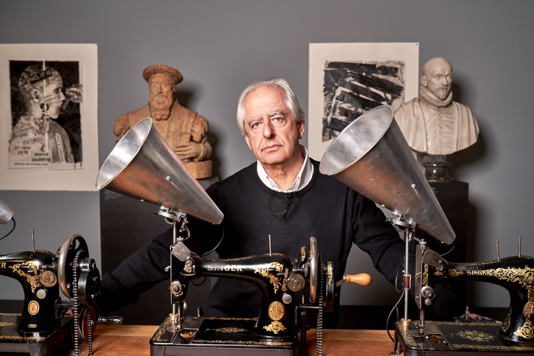 a man sits at a desk with various artworks surrounding him