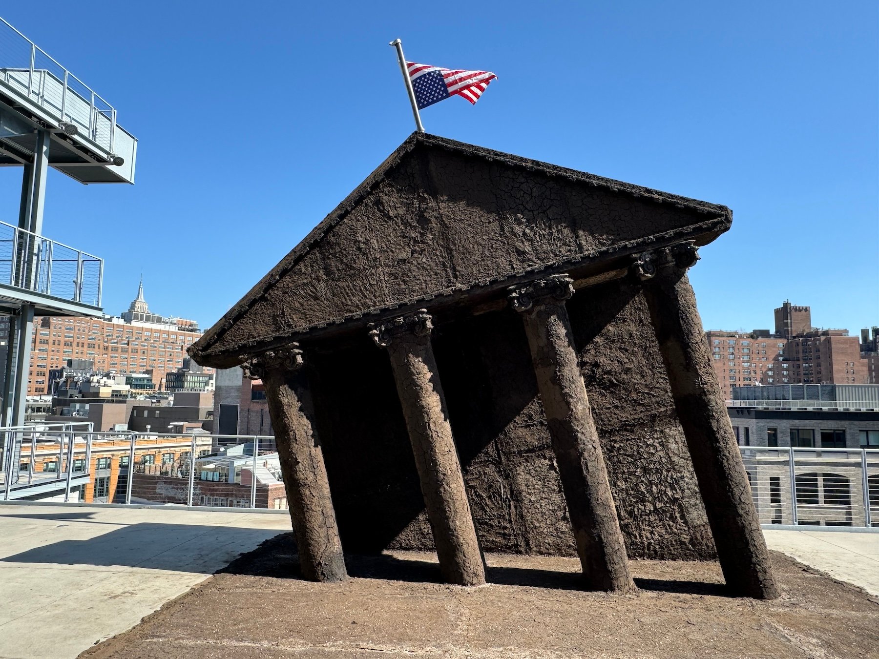 An image of a tilted black sculpture of the north face of the White House flying an upside-down American flag