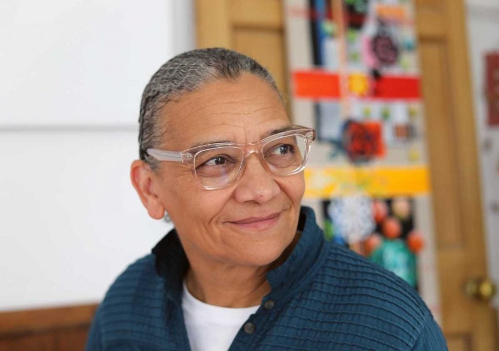 Picture of artist lubaina himid wearing glasses and smiling while standing in her studio