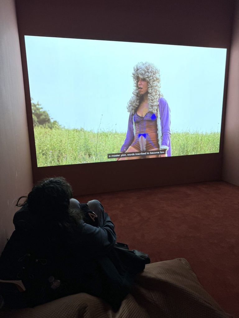 A person watches a video featuring a woman in a field in a wig