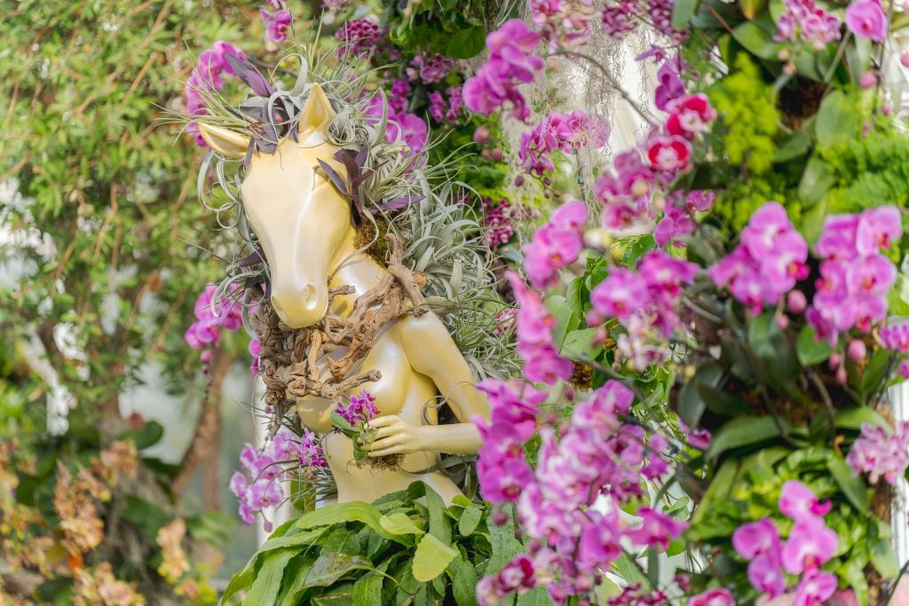 a golden sculpture of a horse hybrid creature is adorned in orchids 