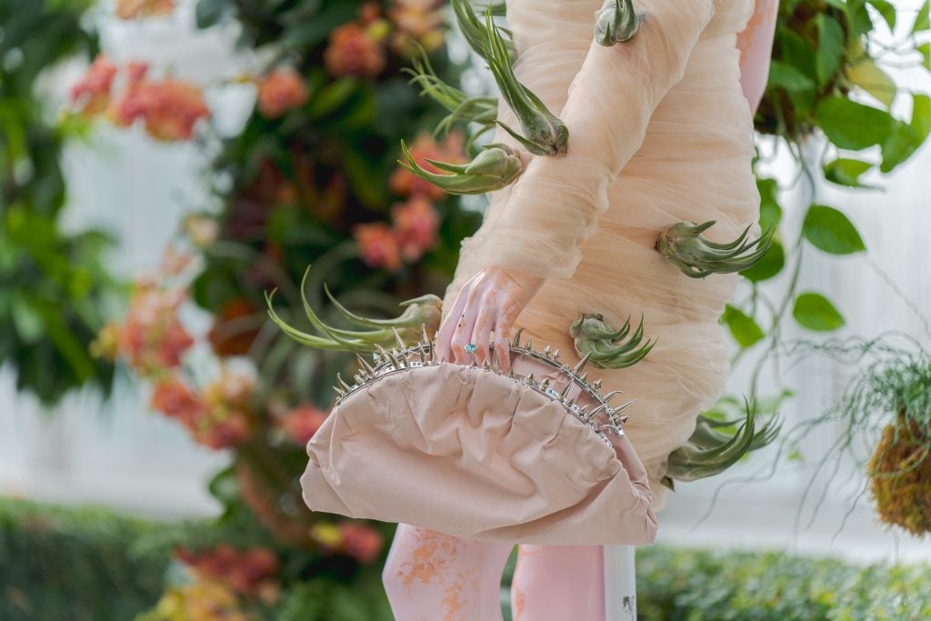 a close-up view of a pink dress adorned with spiky orchids and a handbag that resembles a Venus flytrap. 