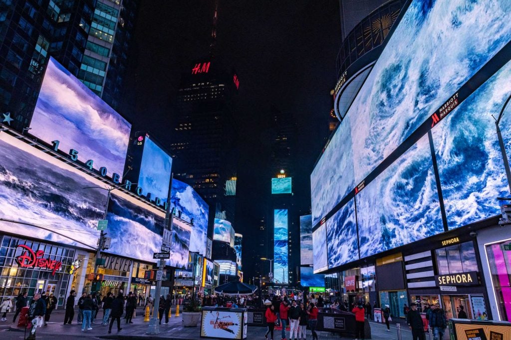 Multiple video screens show images of storms in the center of times square in manhattan