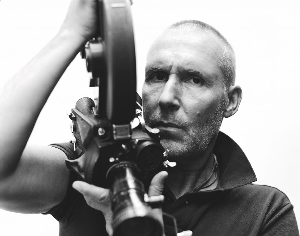 Black and white photo of photographer Michel Comte holding a film video camera.
