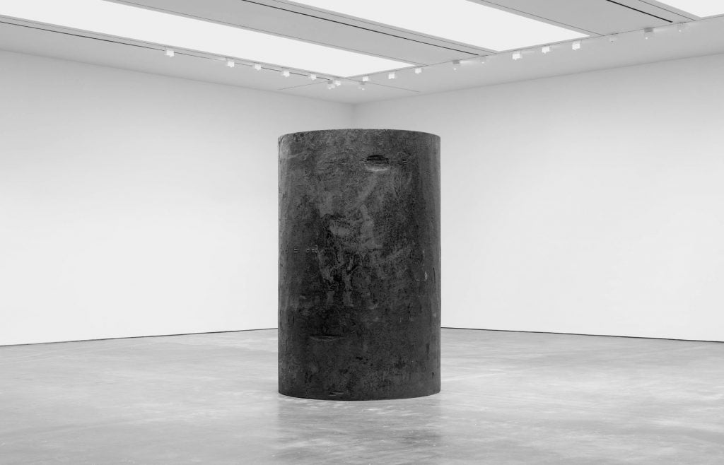 a large dark round structure sits in the middle of a white gallery space