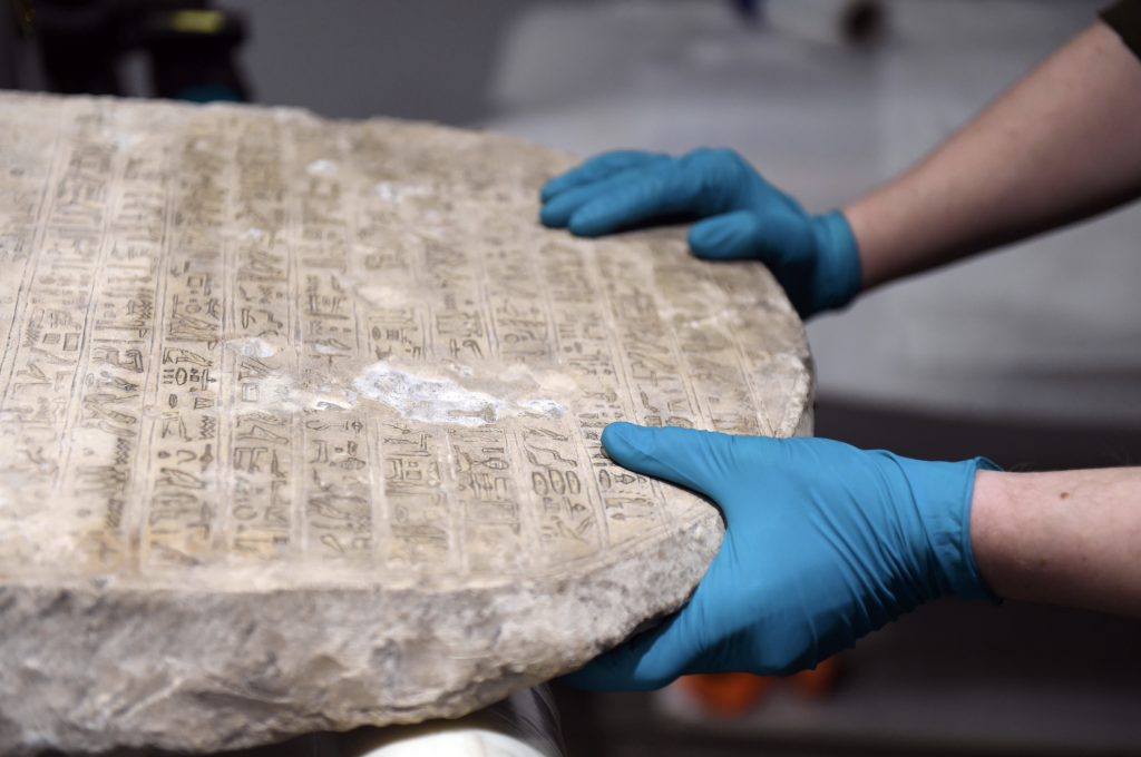 A conservator's hands grasping an ancient Egyptian stone stela.