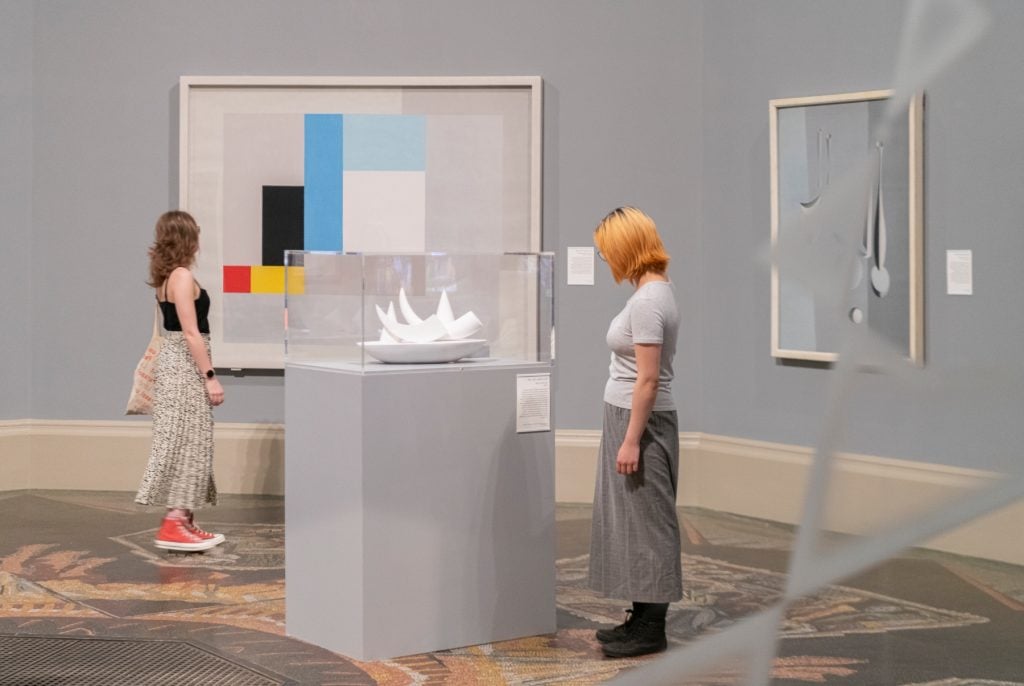 Two women walk through a gallery filled with paintings and sculptuers at Tate Britain.