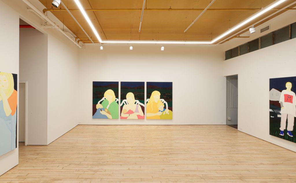 In a color photo, spare paintings of people hang on the white walls of a gallery.