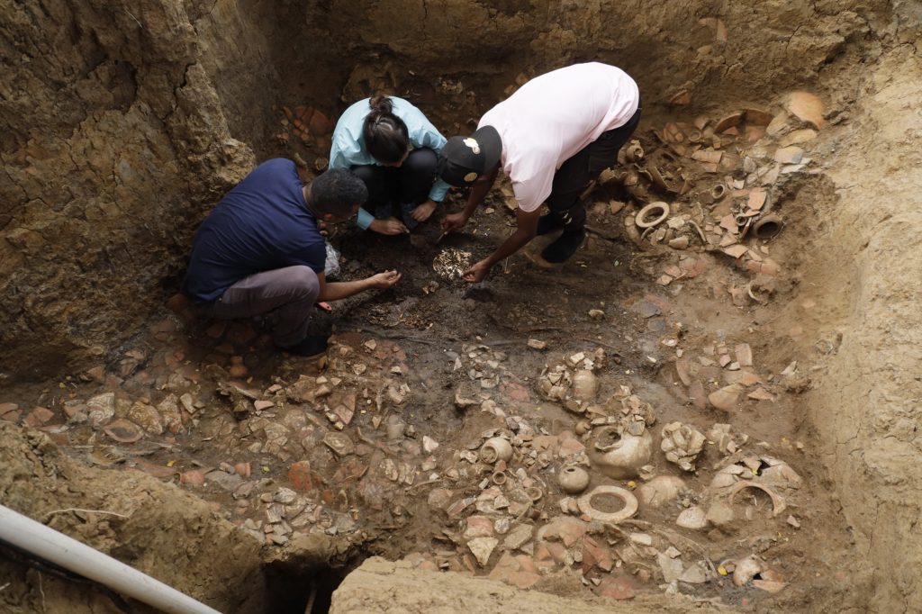 Three people excavating a tomb in Panama, which is filled with ceramic shards.