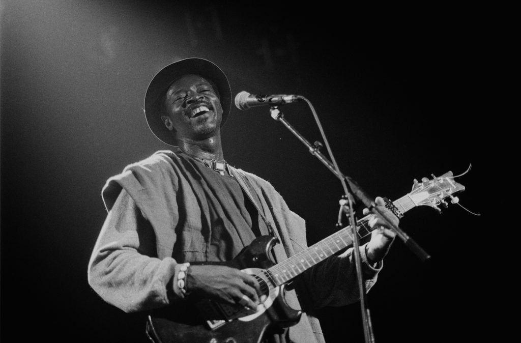 A spotlight shines on Malian guitar player Ali Farka Toure as he performs in front of a microphone.
