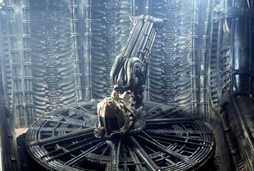 A spaceship lined with tubes, at the center of which is a large contraption occupied by an alien.