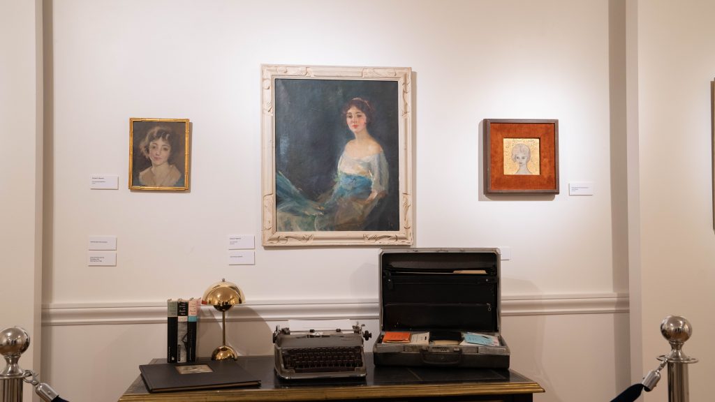 A gallery show installation featuring Anaïs Nin's original typewriter in front of three portraits painted of her