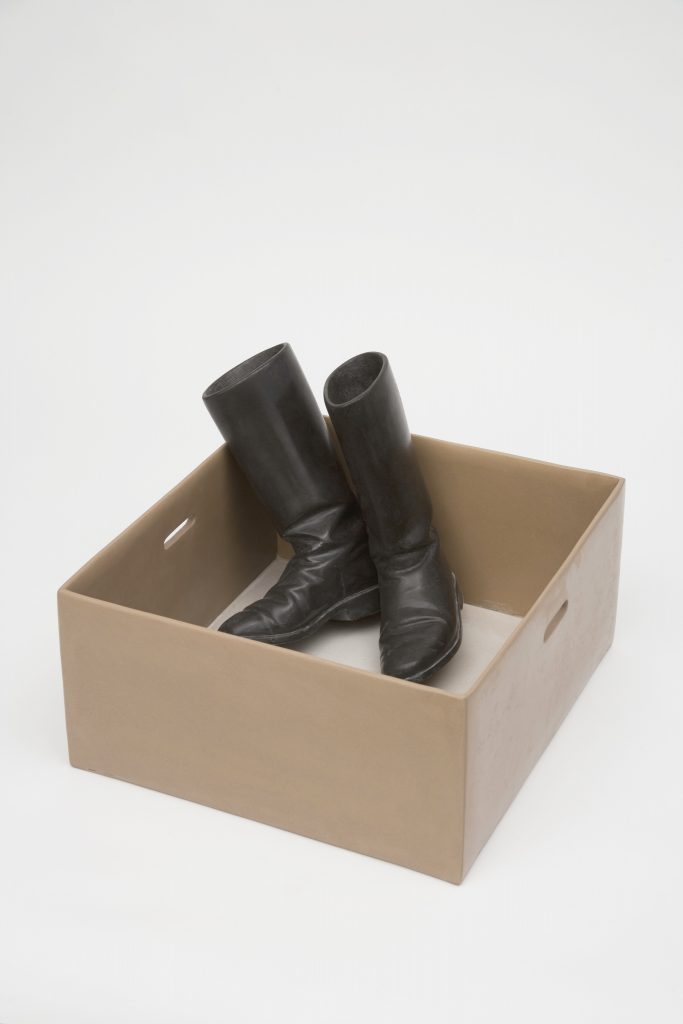 Pair of brown-black riding boots in brown cardboard box, but are in fact made out of stone.