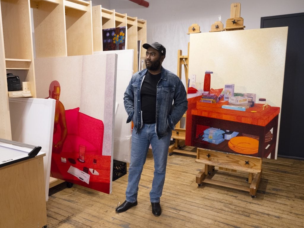 Artist standing in his studio surrounded by partially finished paintings.