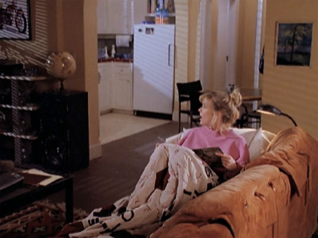 A woman lying on a couch with a quilt covering her knees.