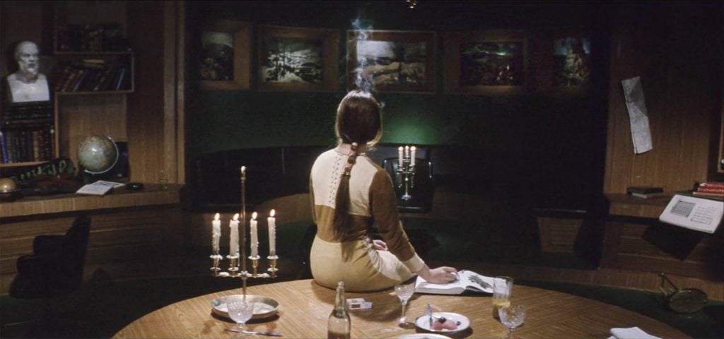 A still from the film Solaris, depicting a woman with her back to us, observing four painted landscapes on a wall.