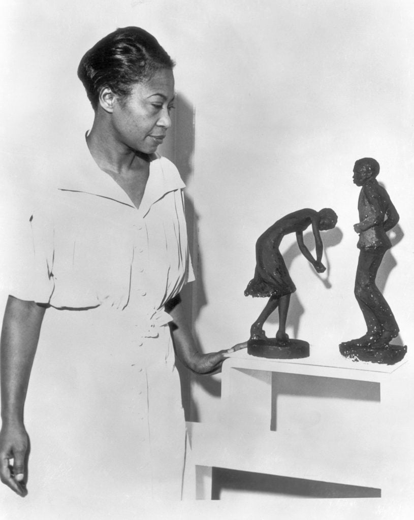 A woman, artist Augusta Savage, standing alongside two of her figurative sculptures.