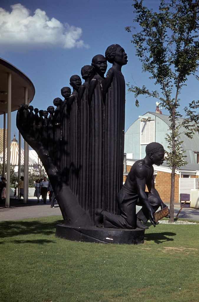 A vintage, colorized photo of Augusta Savage's black plaster sculpture of a harp where 12 singers emerge from a hand, shown on view at the World's Fair of 1939 in Queens, NY