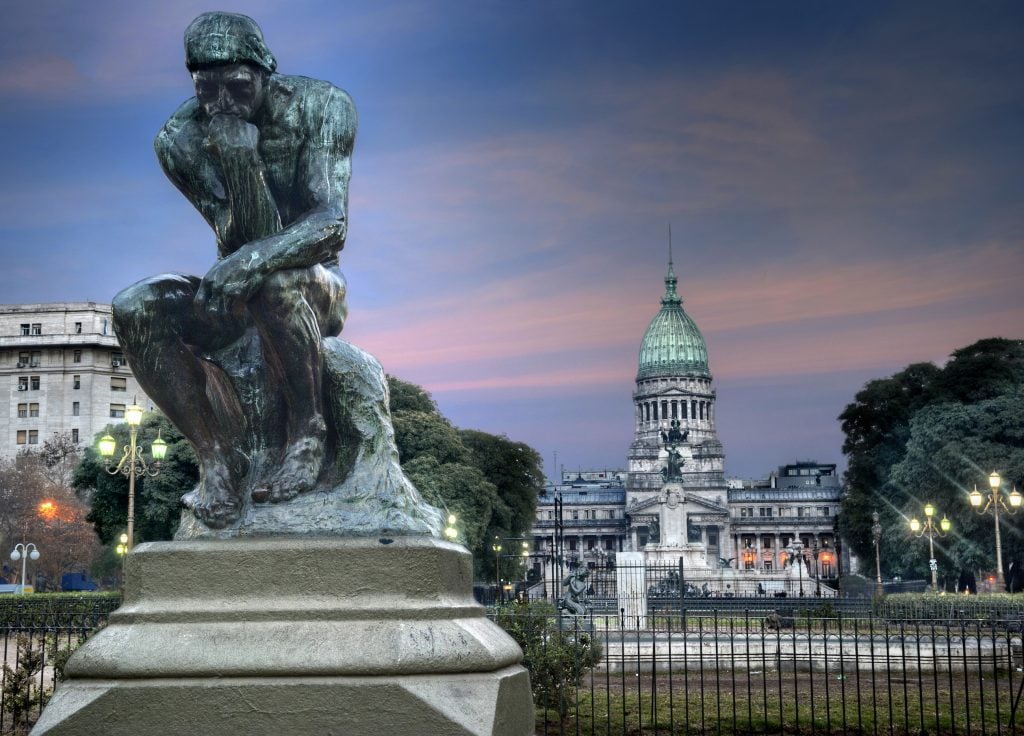 A copy of Auguste Rodin's sculpture The Thinker in Buenos Aires against a colorful sky