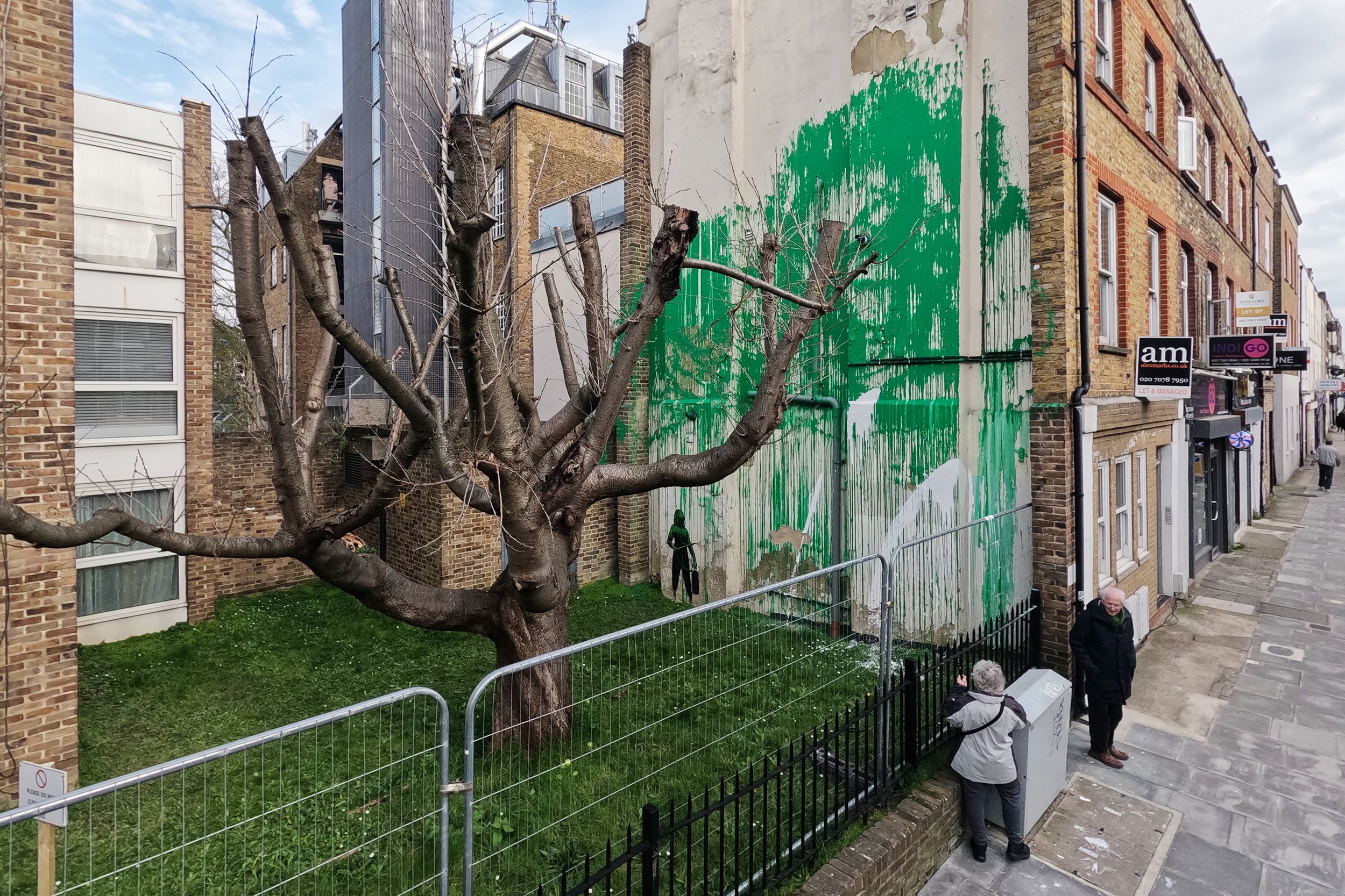 Two people looking at a green-colored mural, which has been defaced with splashes of white paint.