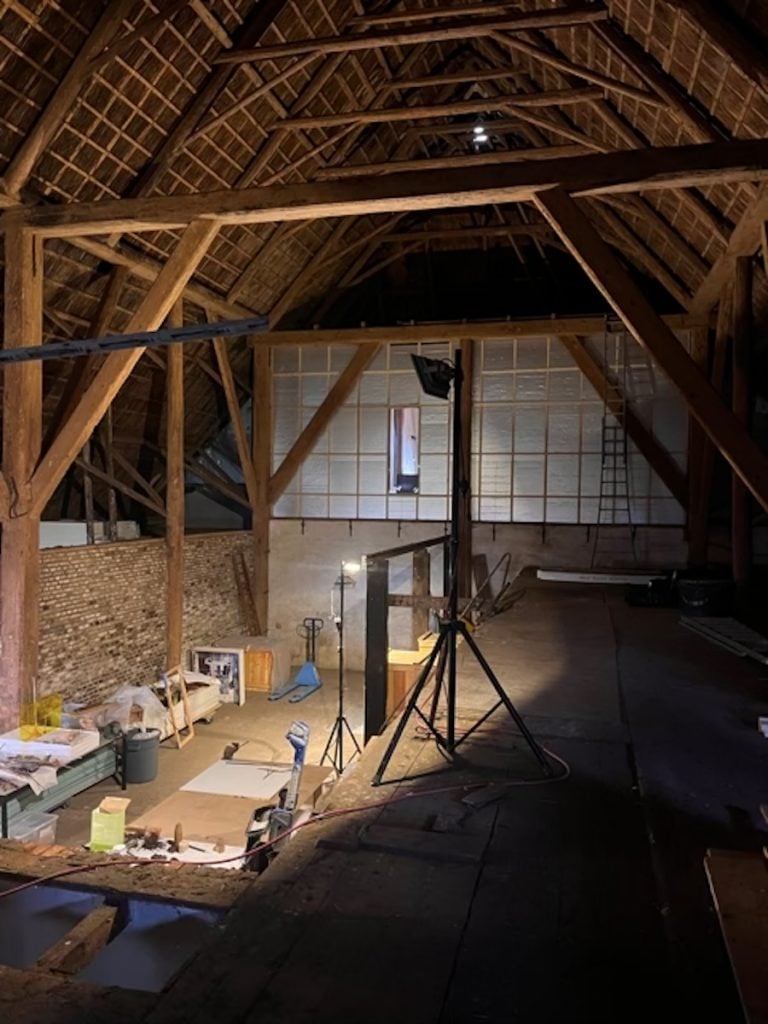 The image is of a room with a wood ceiling and stone walls. The room features beams, walls, and a roof made of lumber. It has an attic-like feel with a wooden floor.