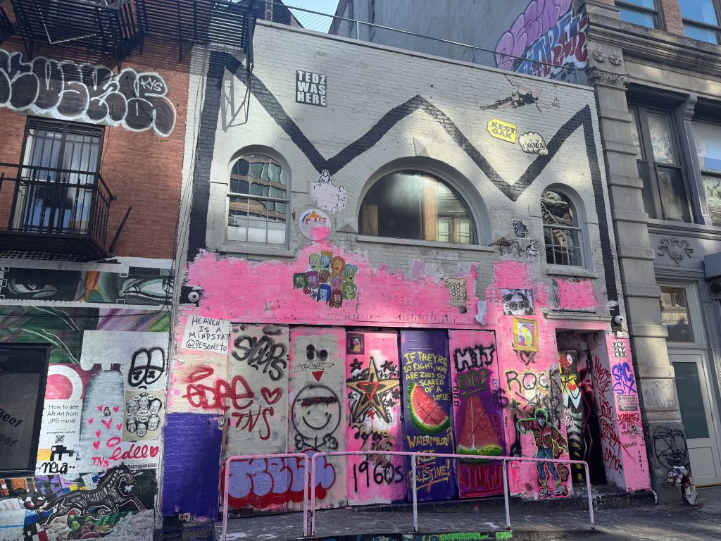 The facade of a building covered in pink paint, with graffiti tags painted over.