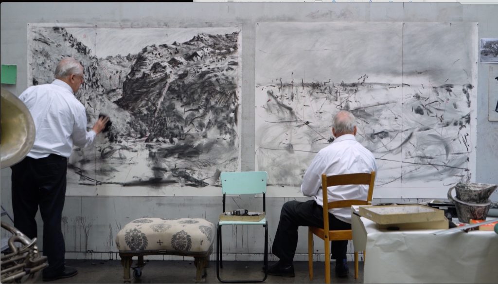 the same man appears twice, drawing an artwork on the wall
