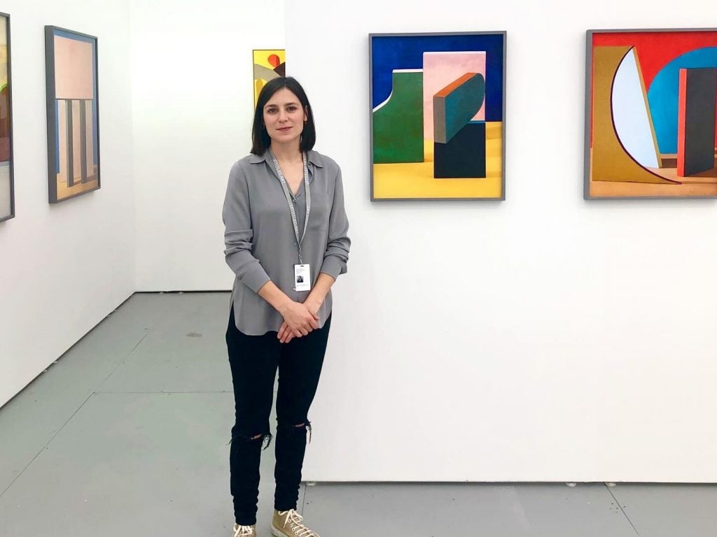 The author stands in front of two colorful abstract paintings at a gallery booth.