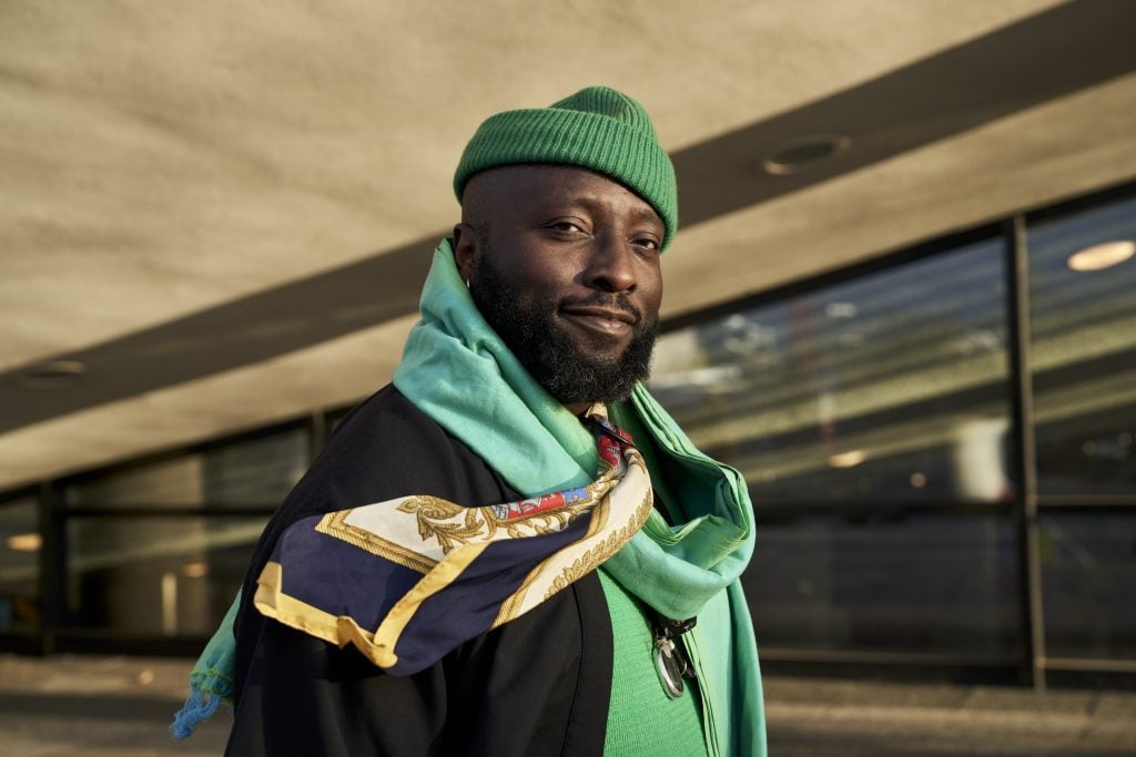 A Black man in green cap and scarf poses for the camera