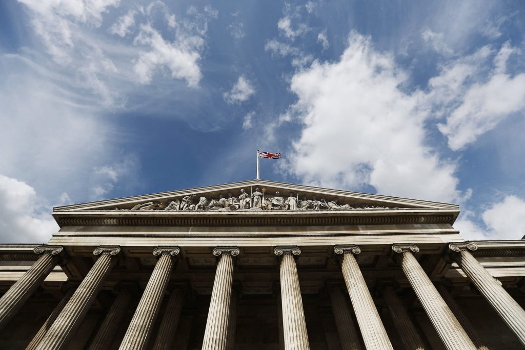 The facade of the British Museum, featuring Greek columns and a triangular pediment, seen against a blue sky.