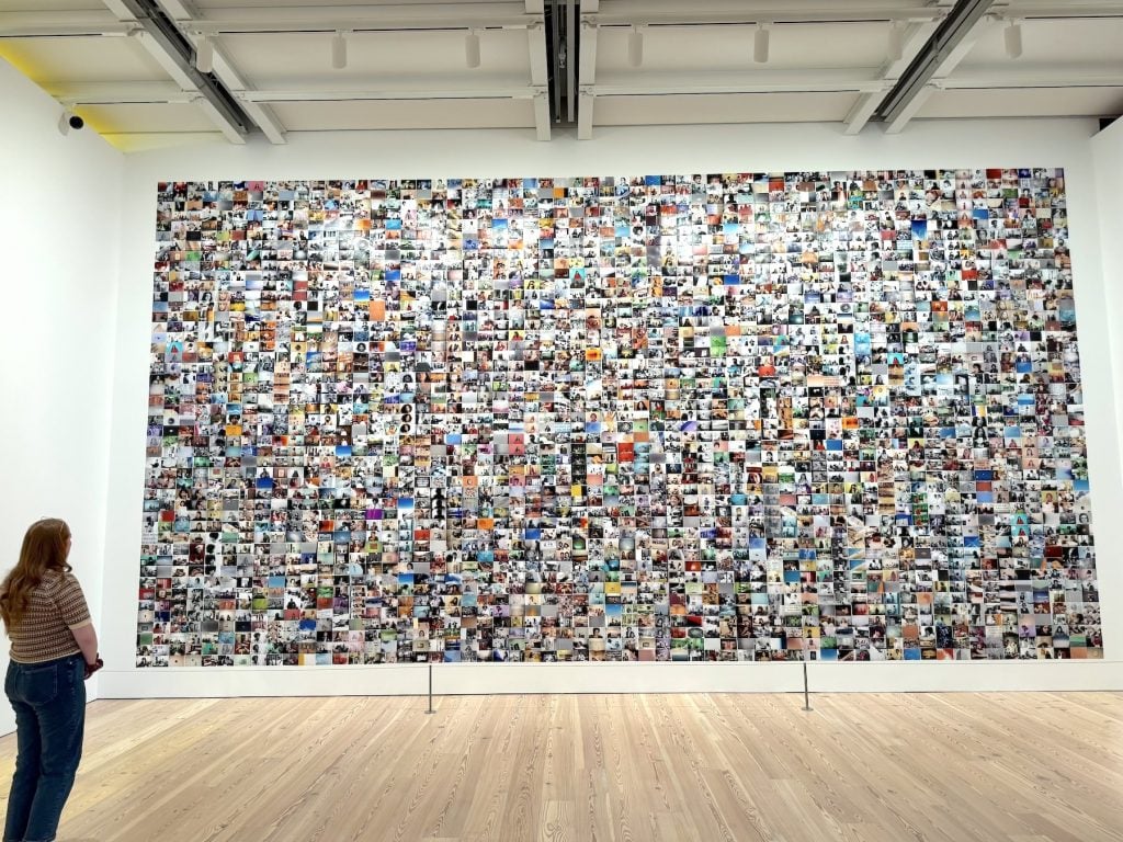 A woman looks at a wall covered in a dense photographic mural
